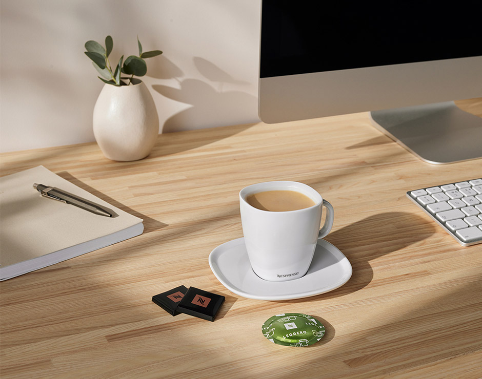 Taza de café blanco encima de una mesa con un ordenador y teclado